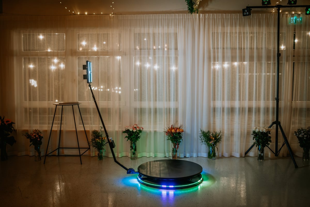 A 360-degree photo booth setup with LED lights and a rotating platform, surrounded by floral arrangements