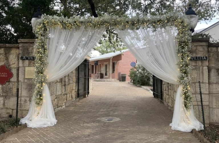 Elegant white draped archway with greenery at a brick building entrance for an outdoor event.