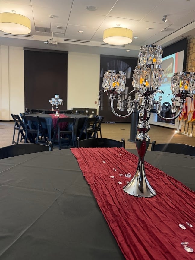 Elegant banquet hall with crystal chandeliers, red runner carpet, round tables with blue chairs, and modern ceiling lights